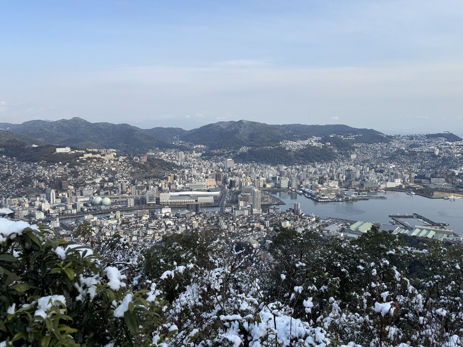 雪をかぶった木々越しに見下ろす長崎駅周辺と長崎港